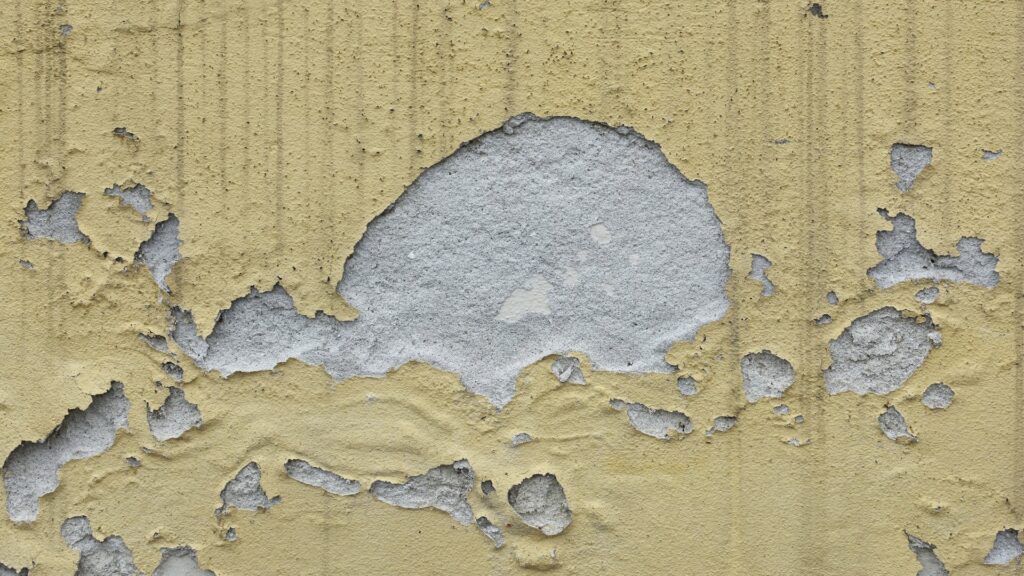 Close-up of a wall with peeling yellow and gray paint