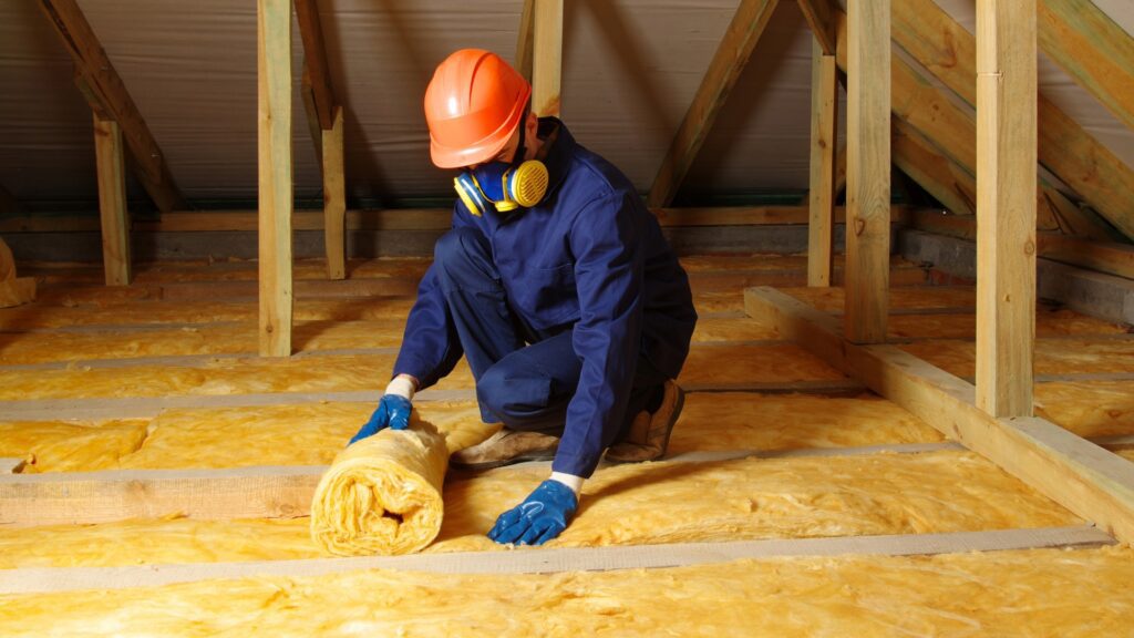 Worker installing insulation in an attic wearing protective gear
